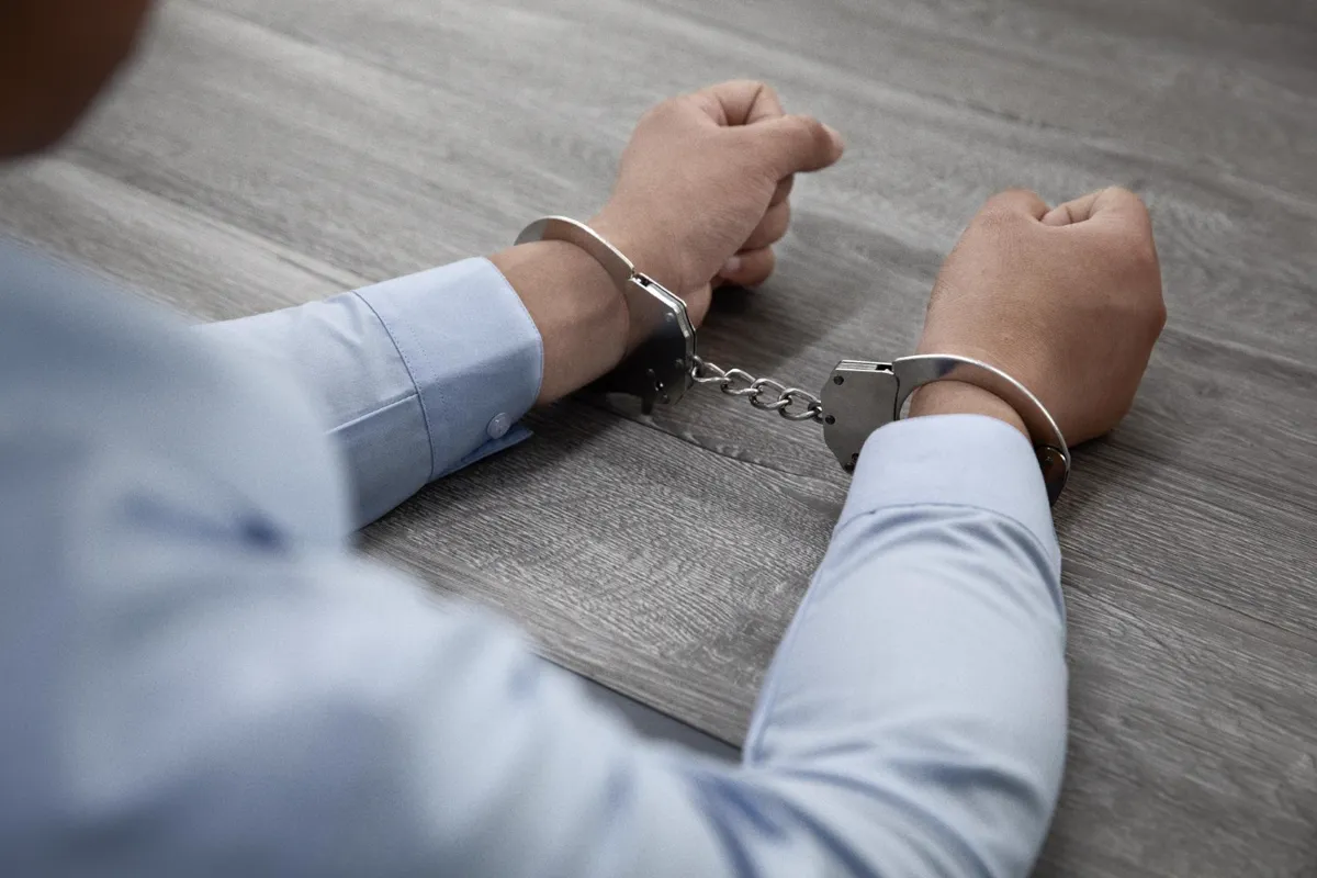 Persona detenida con las manos esposadas sobre una mesa