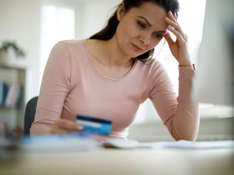 Mujer preocupada revisando sus cuentas con una tarjeta bancaria
