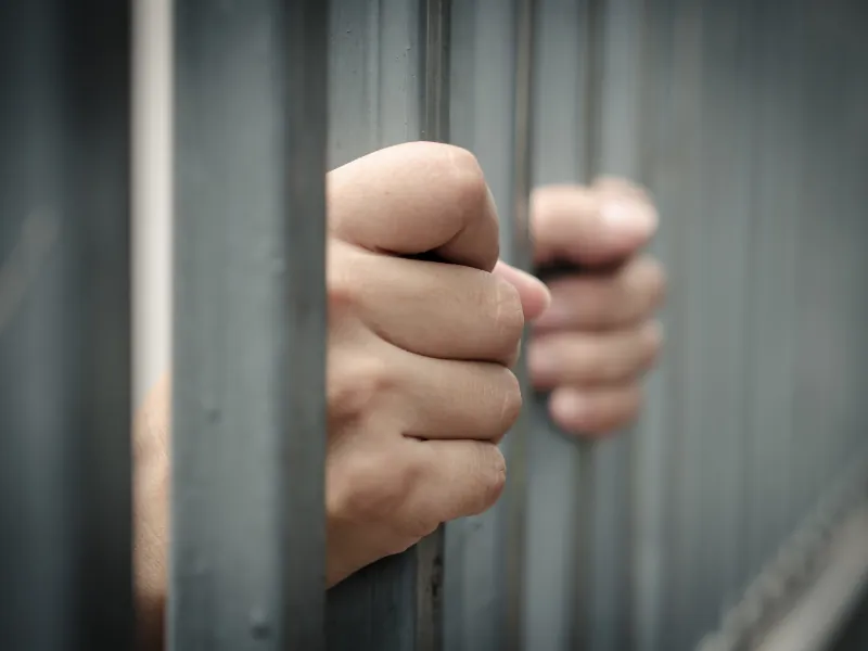 Manos de una persona agarrando los barrotes de una celda